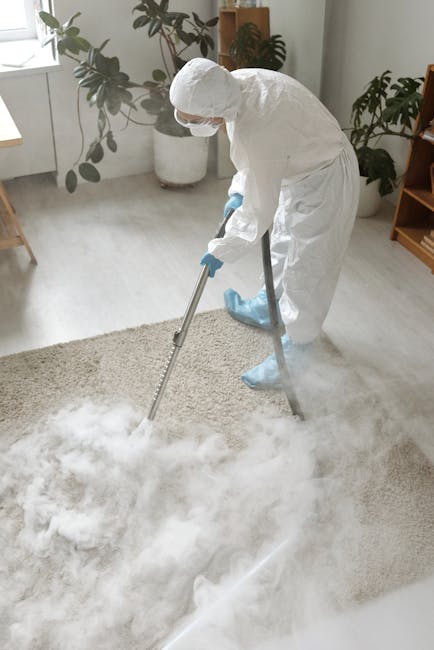 A person in casual attire, including white sneakers and blue jeans, is using a yellow and black vacuum cleaner with a long hose attachment to deep clean a traditional patterned carpet in a room with w