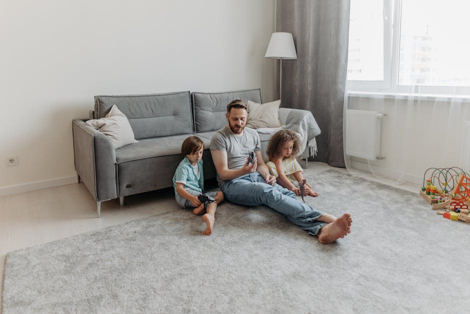 A person dressed in full protective gear, including a white suit, gloves, and blue shoe covers, is performing carpet cleaning in a bright, well-lit room. The individual uses a professional vacuum or e